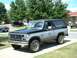 1982 Ford Bronco - A two-tone black and silver Ford Bronco is parked on a driveway, with other vehicles visible in the background.