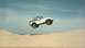 1990 Ford Bronco - A white Jeep Wrangler is captured mid-air, soaring over a sandy landscape with a small red flag trailing behind it.