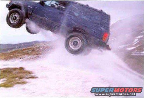 Dark SUV mid-air jump over a snowy hill, kicking up snow
