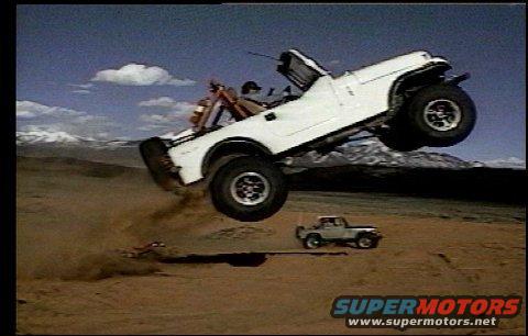 White off-road vehicle airborne over desert terrain, with another vehicle on the ground