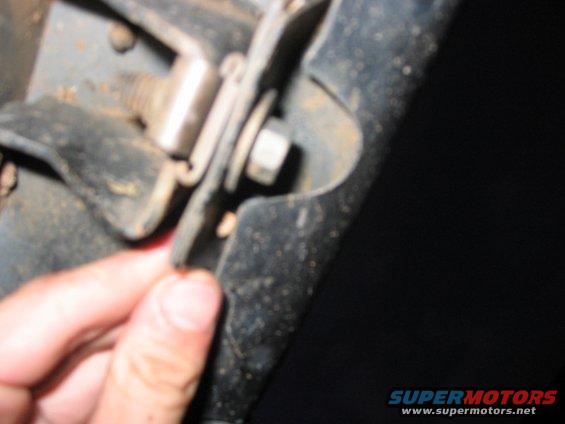 Close-up of a rusty metal bracket with a bolt and nut, held by a hand