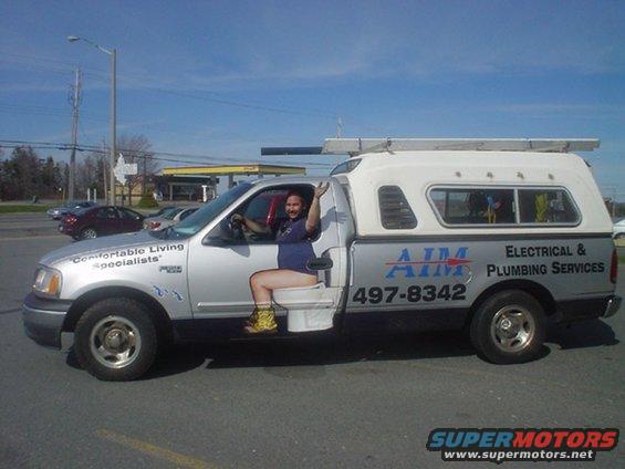 Silver pickup truck with a toilet in the driver's seat and plumbing company decals