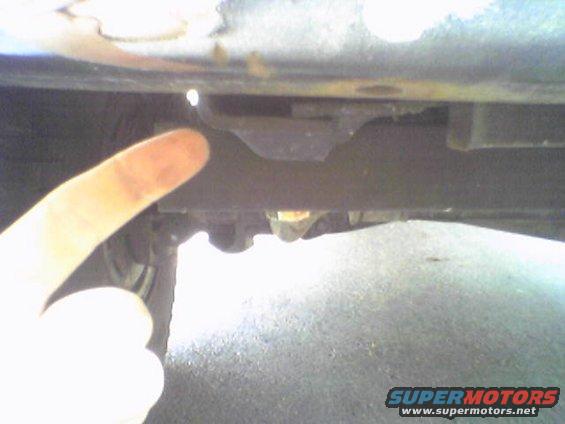 Undercarriage of a vehicle with a finger pointing to a metal bracket