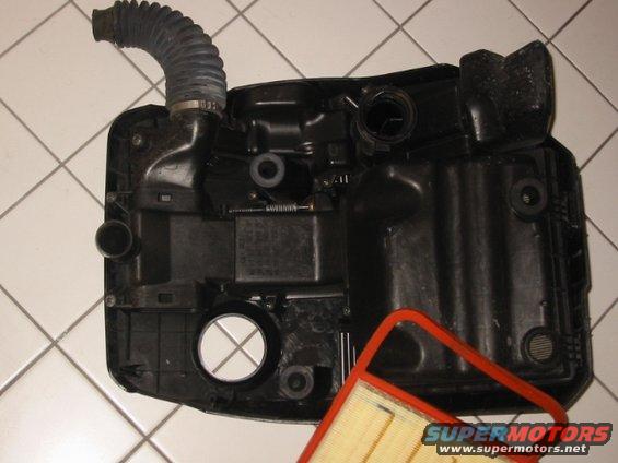 Volkswagen air filter housing with intake hose attached, and a new air filter element. The housing is black plastic with various clips and mounting points