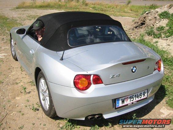 Silver 2003 BMW Z4 convertible with black soft top, rear 3/4 view, parked on dirt with grass