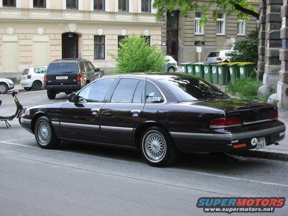 Dark 1992 Ford Crown Victoria sedan, rear 3/4 view, parked on street, some damage on rear bumper
