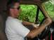 1988 Ford Bronco - A man wearing sunglasses drives a vehicle, with dense green foliage visible through the window.