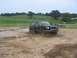 1988 Ford Bronco - A black 1988 Ford Bronco navigates a muddy track, kicking up water and dirt.