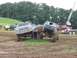 1988 Ford Bronco - Two heavily modified trucks are positioned in a muddy outdoor area with trees in the background.
