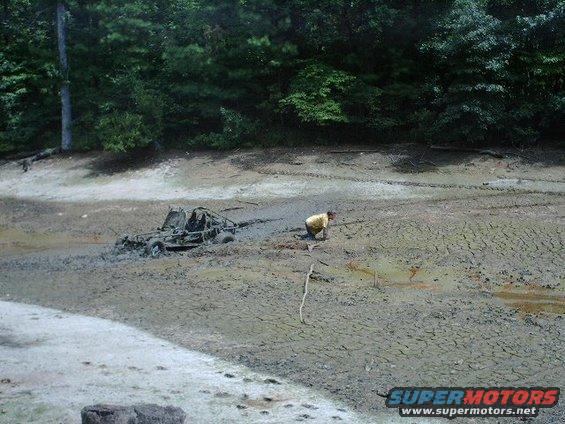 Off-road buggy stuck deep in mud with a person nearby