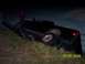 1994 Ford Bronco - A black pickup truck lies overturned on its side in a grassy area at night, with two individuals observing the scene.