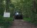 1988 Ford Bronco - A black 1988 Ford Bronco navigates a dirt path through a dense forest, marked by a sign indicating 'The New Trail'.