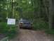 1988 Ford Bronco - SUV drives down a wooded dirt road next to a sign indicating a new trail.