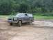 1988 Ford Bronco - A dark-colored Ford Bronco navigates a muddy terrain with trees lining the horizon.