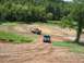 1988 Ford Bronco - Two trucks navigate a challenging muddy track surrounded by lush green trees.