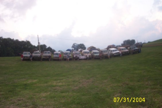 Line of trucks and SUVs parked on a grassy hill under a cloudy sky