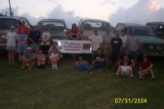 Group of people posing in front of several trucks at an outdoor event