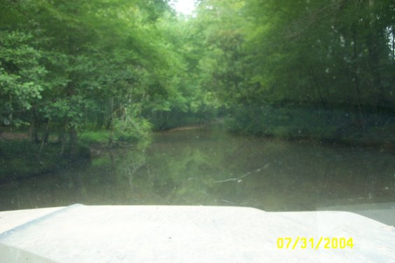 White dashboard and windshield view of a calm body of water surrounded by trees, with a date stamp of 07/31/2004