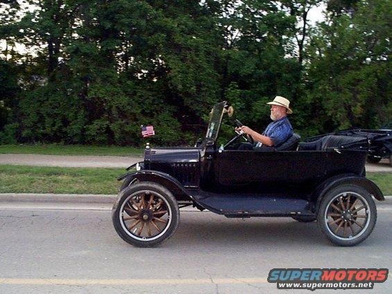 Black antique car with wooden spoke wheels and a man wearing a hat driving