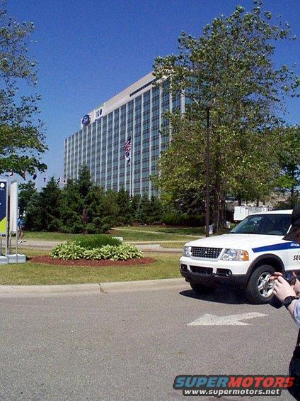 White Ford Explorer SUV with blue stripe, security markings, parked in front of a large office building