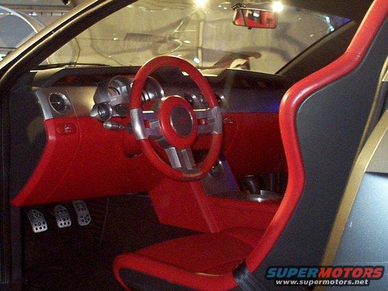 Car interior showing red seats, dashboard, and steering wheel. Pedals visible on the floor