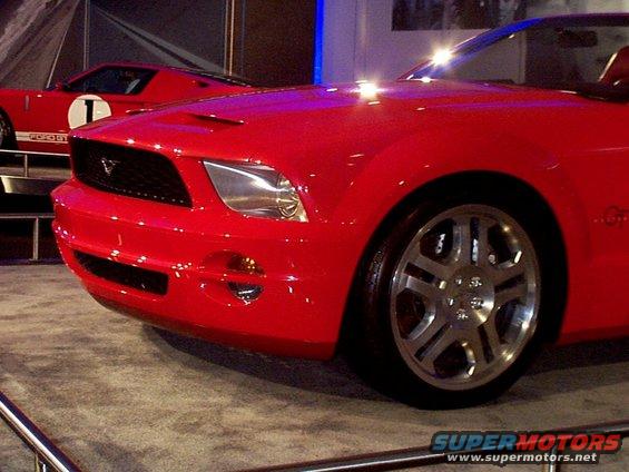 Red Ford Mustang with a black grille and silver wheels. Another red car is behind it