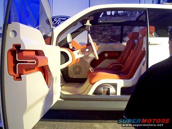 Interior of a concept car with orange seats and white trim. Door is open showing a cutaway view of the door panel