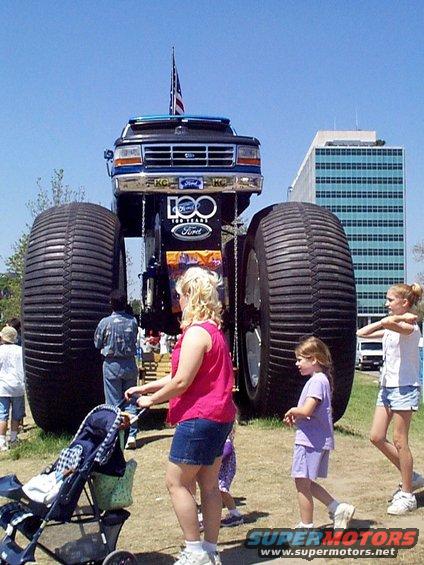 Monster truck with huge tires and Ford logo, people around