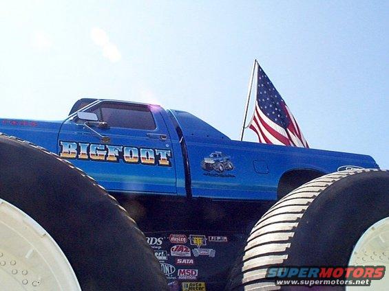 Blue Bigfoot monster truck with large tires, American flag in bed, seen from low angle