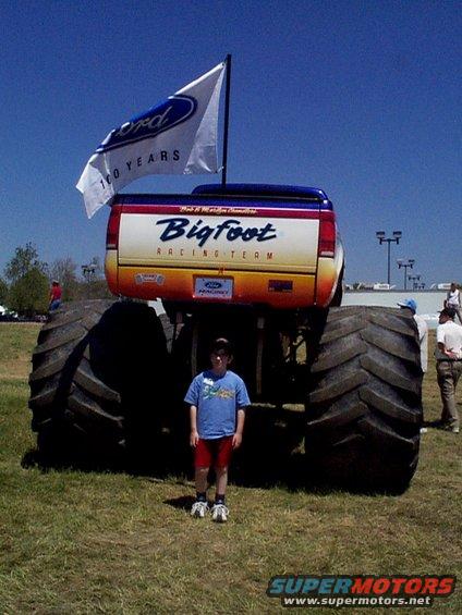Kid standing in front of Bigfoot monster truck with Ford 100 years flag