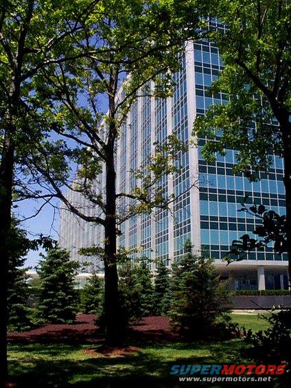 Tall office building with blue windows surrounded by green trees