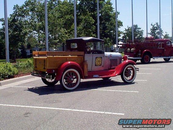 Antique red and silver pickup truck with wooden bed parked next to a red fire truck