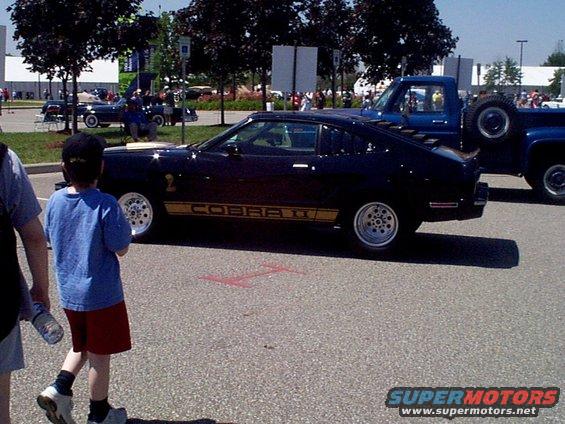 Black Ford Mustang Cobra II with gold stripe on side, parked next to a blue pickup truck