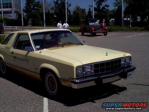 Yellow 1978 Ford Fairmont Futura coupe parked on asphalt, front quarter view. Another vintage car is in the background