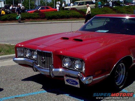 Red 1970s Ford car front view, chrome grille, dual hood scoops, Ford license plate