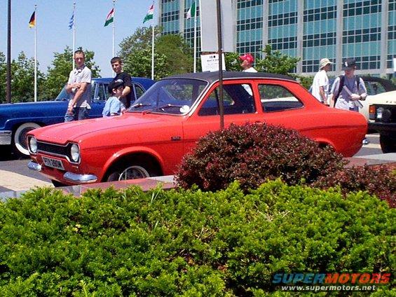 Red coupe with black roof parked next to a blue car, people standing around
