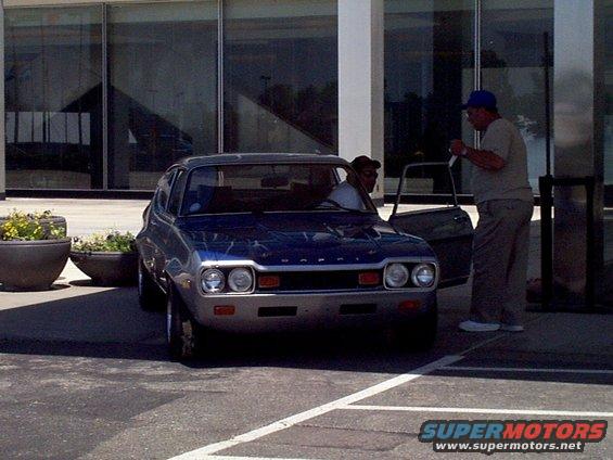 Blue hatchback car with dual headlights and chrome bumper parked outside a building