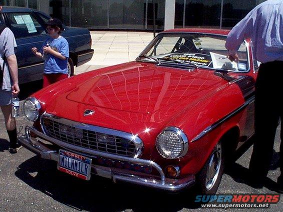 Red 1961 Volvo P1800 coupe with custom license plate MILNNILR parked next to a dark blue car