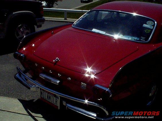 Rear of a red Volvo coupe with chrome bumper and license plate MILNMILR. Another dark vehicle is parked to the left