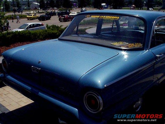 Rear view of a blue classic car with a "FOR SALE" sticker on the back window