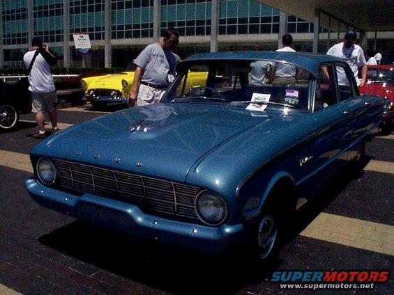 Blue classic sedan with chrome grille and trim. Yellow and red cars in background
