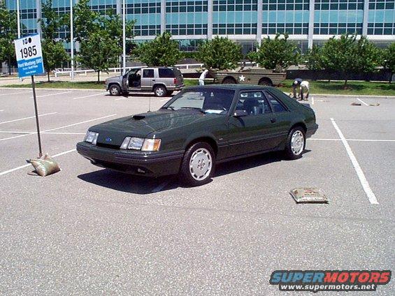 Dark green 1985 Ford Mustang coupe parked in a lot, front 3/4 view
