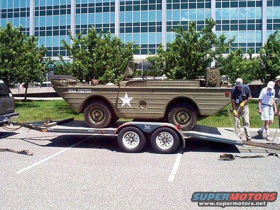 Olive drab amphibious military vehicle with white star emblem and USA 7012703 text, on a trailer