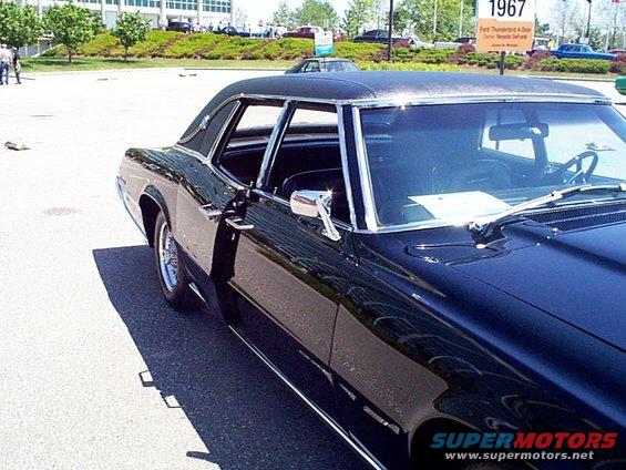 Black coupe with a vinyl roof, chrome trim, and a side mirror. A sign in the background reads '1967 Ford Thunderbird'