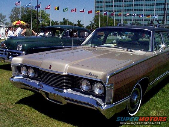 Wood-paneled Mercury station wagon, front end visible. Another classic car is parked behind it