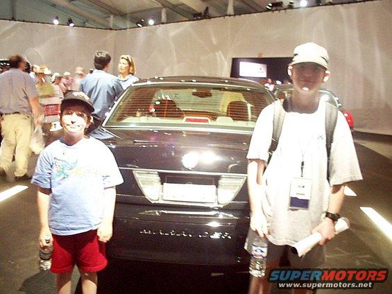 Dark sedan rear view with two boys standing in front