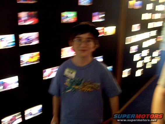 Boy in blue t-shirt with name tag stands in front of a wall of small illuminated images