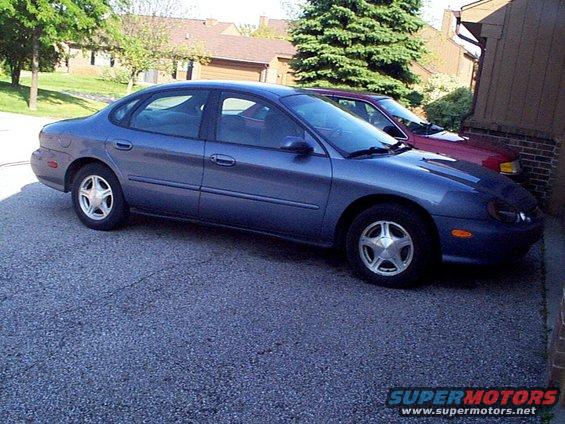 1999 Ford Taurus SE sedan parked outside, side view. Red car behind it