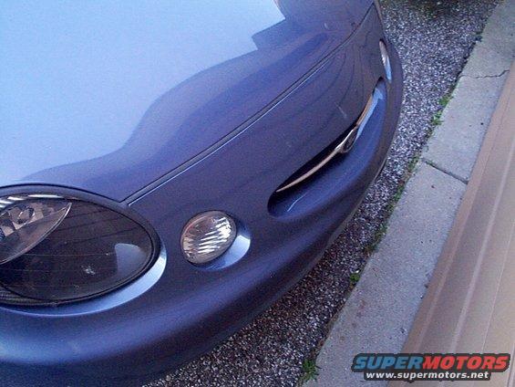 Blue car front corner, driver side headlight and fog light visible, chrome grille accent