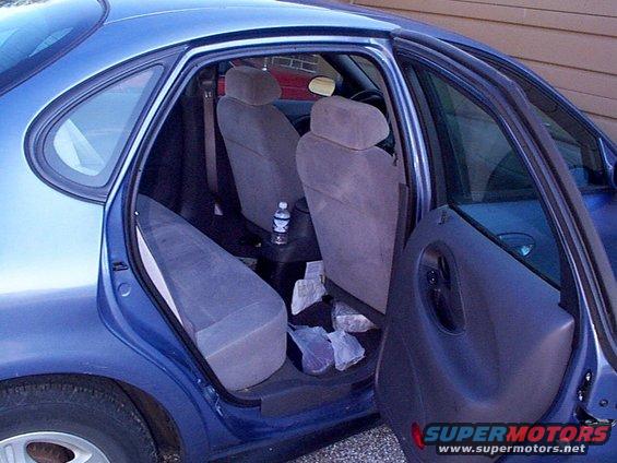 Interior of a blue 1999 Ford Taurus with back doors open. Seats are gray cloth. Water bottle on center console